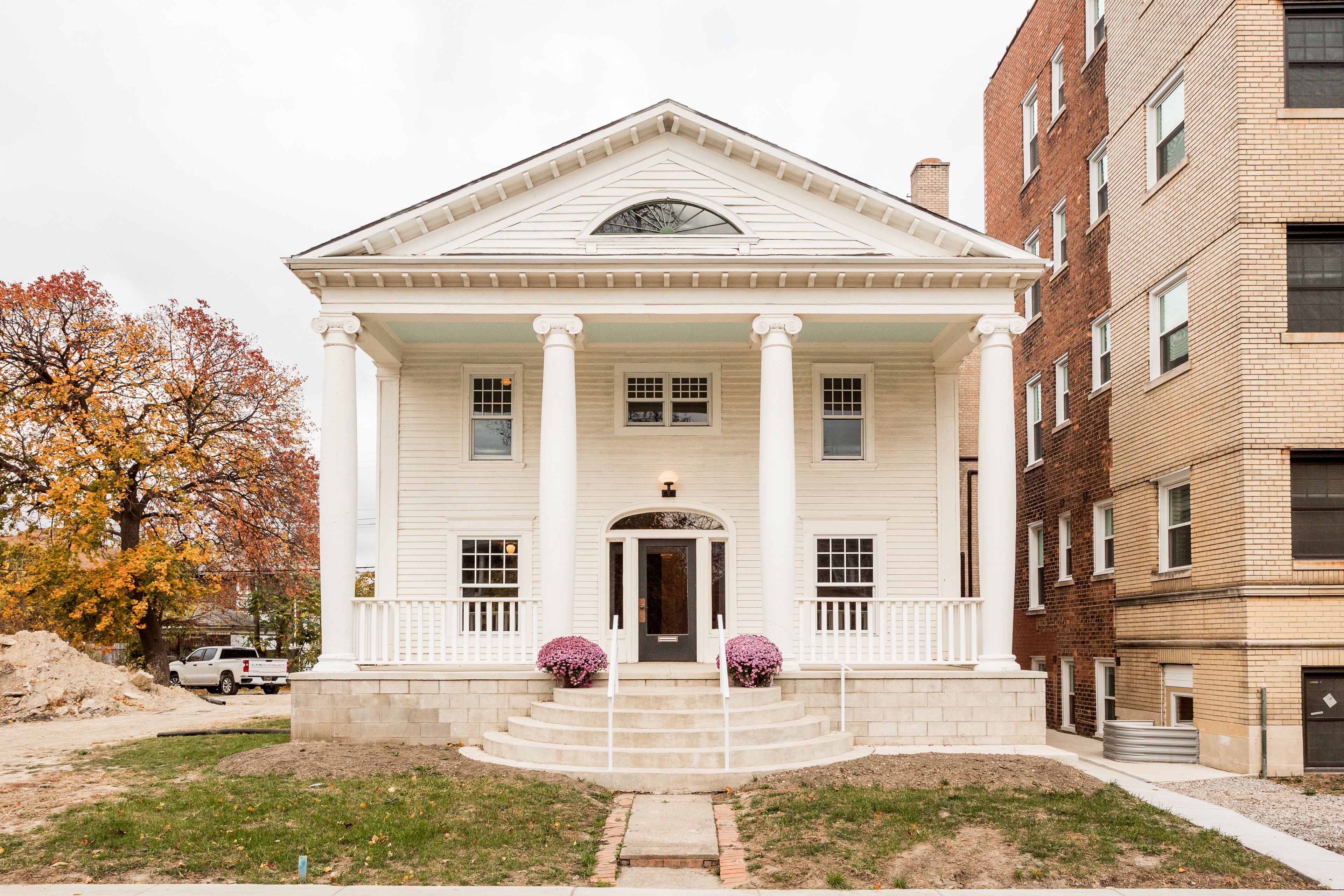 A white house with a porch and a tree in front of it.